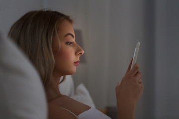 young woman with smartphone in bed at night