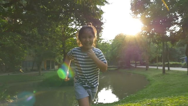 Slow motion shot : Happy Asian little girl running in the park with sunlight