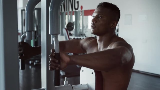 Young athletic man executing reverse machine flies in gym