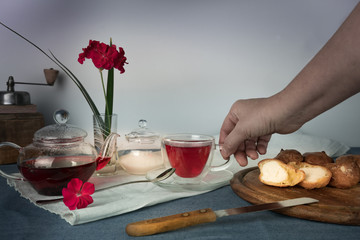 woman's hand with a cup of tea on the table  , scones and geranium flower in  vase
