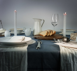 still life. jug, glasses, bun, white candles on a blue tablecloth