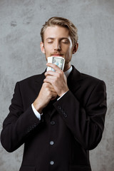 Young successful businessman in suit holding money over grey background. 