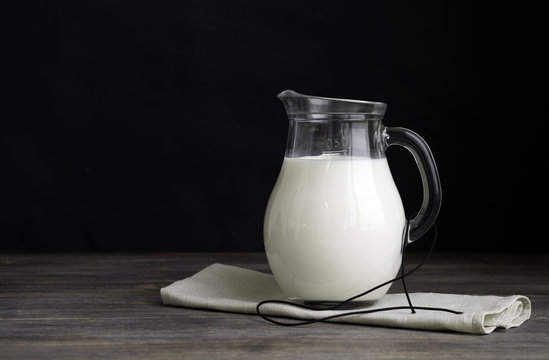 Jug of milk and napkin on a wooden table against black background. Copy space.