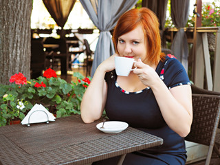 Portrait of attractive plus size redhead woman sitting in a cafe in city park with cup of coffee