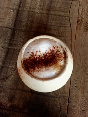 Cappuccino in round cup on wooden table with milk foam and chocolate powder