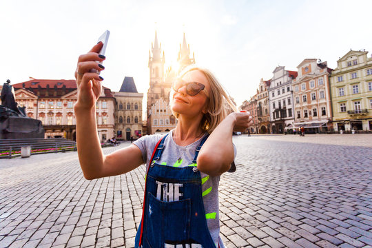 Beautiful young female traveler making self photo on her mobile phone on the background of the Church of Virgin Mary in Old Town Square in Prague. Kostel Panny Marie pred Tynem.