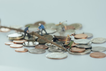 Miniature workmen cutting the tree on pile of coins.
