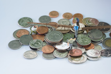 Miniature workmen cutting the tree on pile of coins.