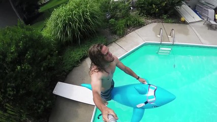 Young man jumps off diving board with inflatable pool float, summer fun, slow motion.