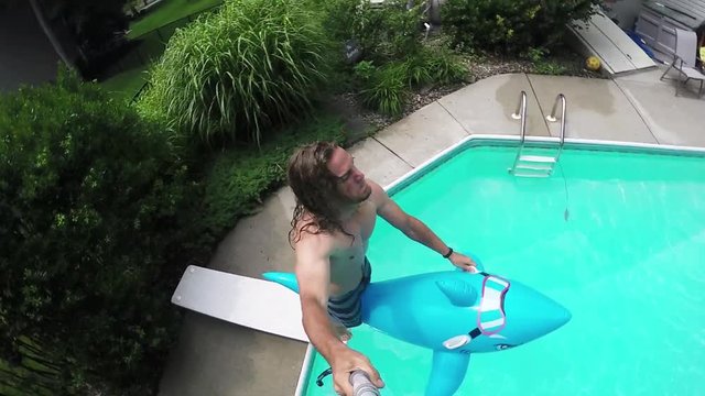 Young man jumps off diving board with inflatable pool float, summer fun, slow motion.