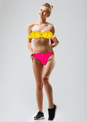 Fototapeta premium Playful blonde girl smiling, covering fake swimwear over white background.