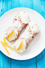 Sicilian Cannoli on white dish and blue wooden table - typical italian pastry with ricotta cheese