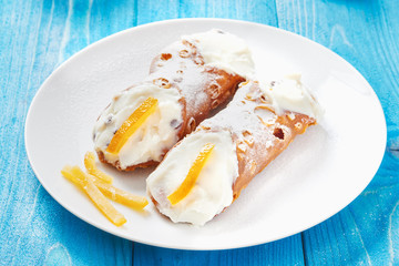 Sicilian Cannoli on white dish and blue wooden table - typical italian pastry with ricotta cheese