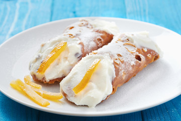 Sicilian Cannoli on white dish and blue wooden table - typical italian pastry with ricotta cheese