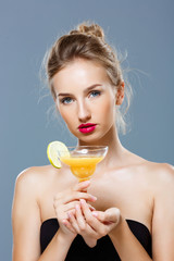 Beautiful blonde naked girl holding cocktail over grey background.