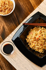 Rice with vegetables on black square dish, chopsticks, soy sauce, dark wooden table