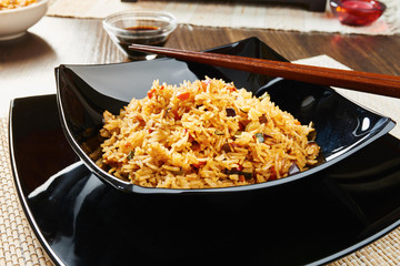 Rice with vegetables on black square dish, chopsticks, dark wooden table