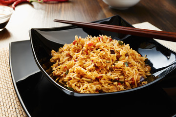 Rice with vegetables on black square dish, chopsticks, soy sauce, dark wooden table