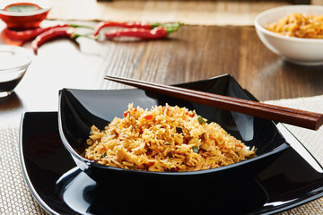 Rice with vegetables on black square dish, chopsticks, soy sauce, dark wooden table