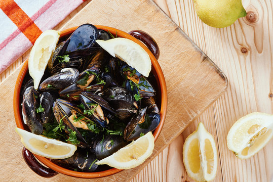 Steamed mussels in a pot, lemons, wooden table