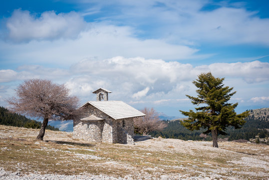 Wintry landscape with a small chapel, two trees and blue sky  on mountain Helmos near Kalavryta town in Greece