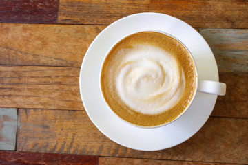 Top view of hot coffee cappuccino cup with milk foam on plank wood table background.