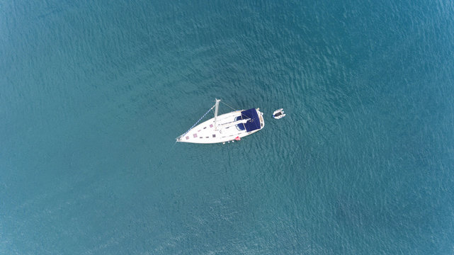 Top view of sailing yacht with a small pontoon floating in the middle of calm sea turquoise, green waters