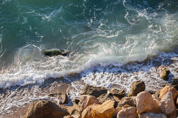 Small waves, sea foam and coastal rocks on sunny day