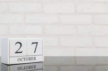Closeup white wooden calendar with black 27 october word on black glass table and white brick wall textured background with copy space , selective focus at the calendar
