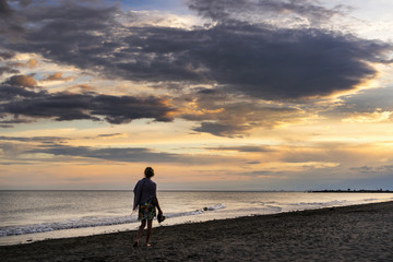 A woman walks alone along a sunset beach shoreline