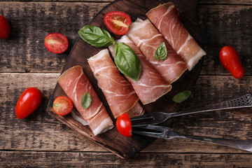 thin slices of prosciutto with mixed with basil, cherry tomatoes on wooden cutting board,vintage...
