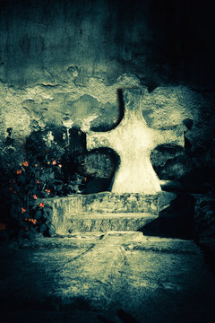 Abandoned grave at dark spooky night on an old cemetery. Tombstone cross next to the ruined church wall. Evil and death concept