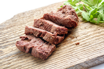 Sliced beef served with fresh greenery on an old rustic wooden chopping board