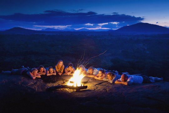 A Group Of People Laying In A Row By A Campfire; Manica, Mozambique, Africa