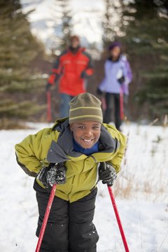 A Boy Holding Ski Poles With His Parents In The Background; Lake Louise, Alberta, Canada