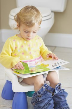 Knoxville, Tennessee, United States Of America; A Young Child Sitting On A Child's Potty And Reading A Book
