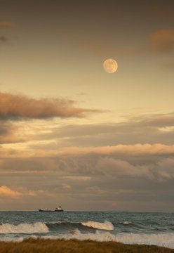 Saltburn, Teesside, England; A Cargo Ship Traveling On The Ocean With The Moon In The Sky