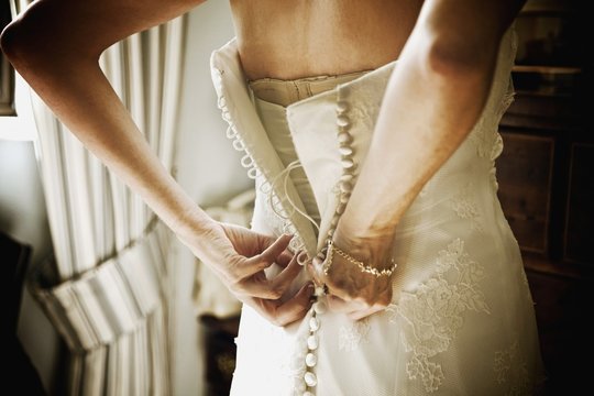 Mid section of a bride buttoning up the back of her white wedding dress