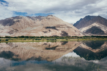 Mountain peaks reflect in water Nubra river