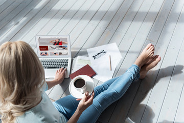 Top view of woman holding coffee cup and using laptop