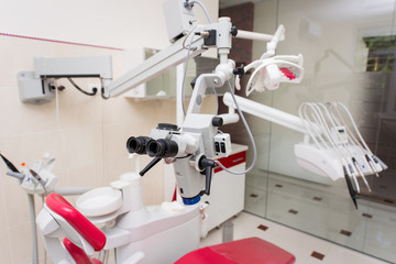 Dental microscope. Unit with top feeding tools, red chair, equipment and other accessories in the modern dental cabinet