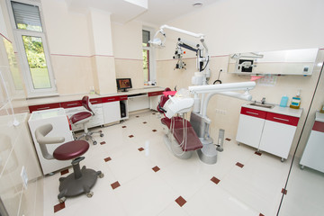 Surgery. Dental office with modern dental units, chairs, equipment, tools, computer and microscope used by dentists. Cabinet in red and white colors
