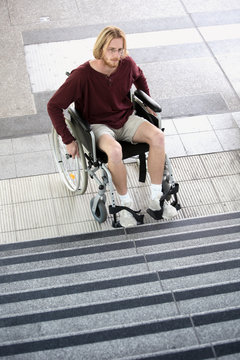 young man in wheel chair in front of stairs looking sad