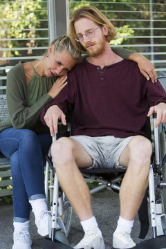 woman hugging man in wheelchair and looking sad