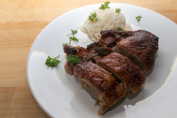 Crispy fried duck breast with rice on a white plate, warm wooden background with copy space
