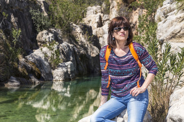 woman with sunglasses resting next to a river in the mountains