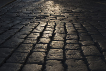 Black cobbled stone road background with reflection of light seen on the road. Black or dark grey...