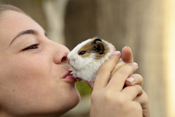 Happy girl with your Guinea pig in the hands, giving kisses. Horizontal capture.