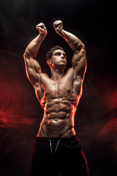 Strong Man Bodybuilder with Six Pack and perfect abs, shoulders, biceps, triceps and chest, personal fitness trainer flexing his muscles in red smoke.