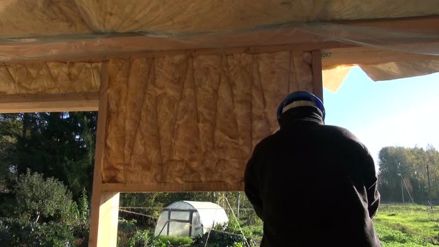 Builder wearing blue helmet insulating house frame with stone wool by fixing it with string